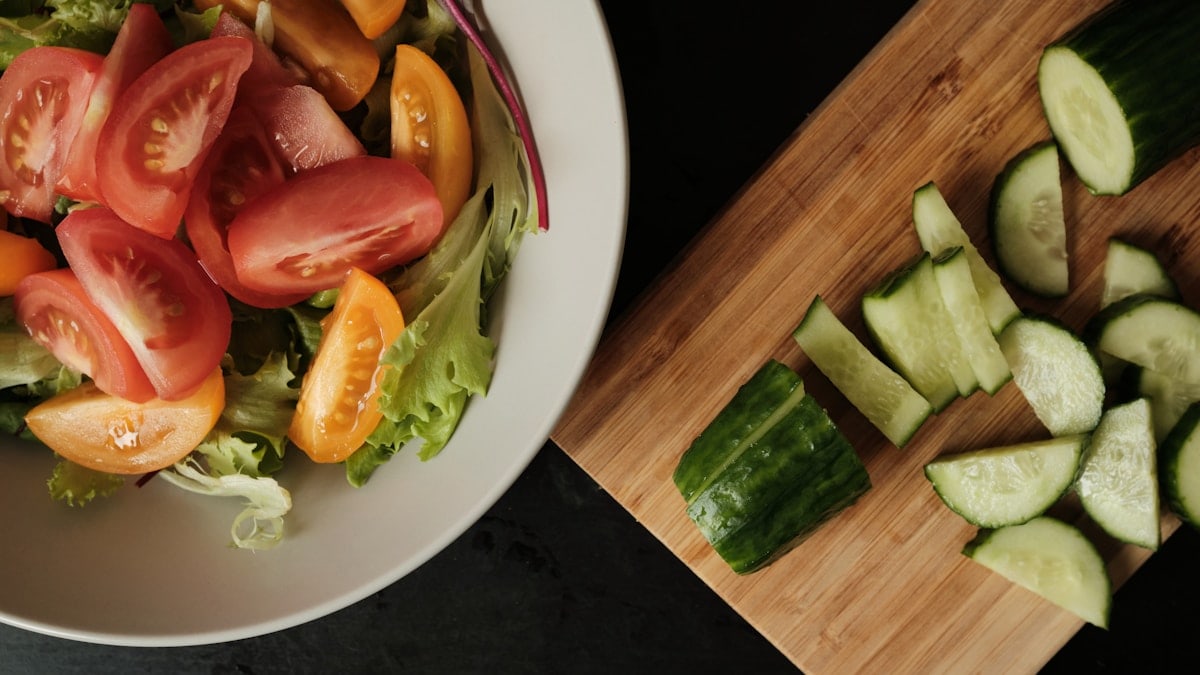 Fresh green salad with cherry tomatoes and sliced cucumber on wooden kitchen board